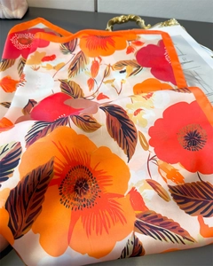 Détail d'un foulard en satin à fleurs montrant la texture soie et les bords oranges