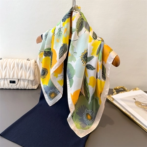 Foulard en soie satinée aux motifs floraux jaunes et verts suspendu sur un cintre