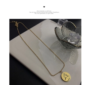 Vue détaillée d'un pendentif pièce avec visage abstrait sur une chaîne dorée chic