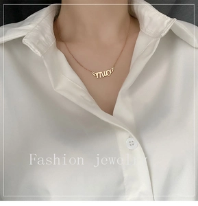 Detail of a minimalist gold necklace with MUO letter pendant on a white shirt model