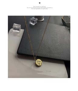 Détail du collier médaille dorée minimaliste avec gravure de visage abstrait sur carte