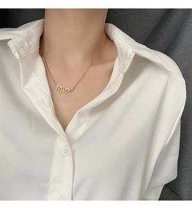 Close-up of a gold titanium necklace with a mio letter pendant worn by a model in white