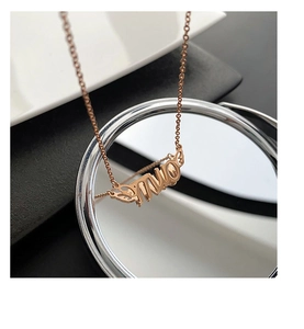 Detail of rose gold lucky letter necklace with wings on a reflective mirror surface