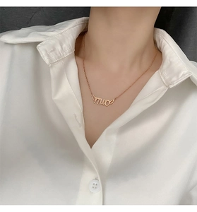 Detailed view of gold Milo letter necklace with wings on a model wearing a white shirt