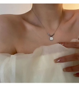 Close-up of minimalist shell smiley face square pendant necklace on female collarbone