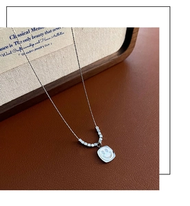 Detail of silver shell smiley face pendant with square beads on a leather surface