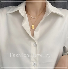Close-up of double-layered gold necklace with natural pearls and a square engraved pendant