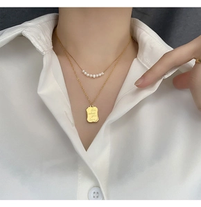 Macro view of gold-plated double-layer necklace with pearls and engraved pendant