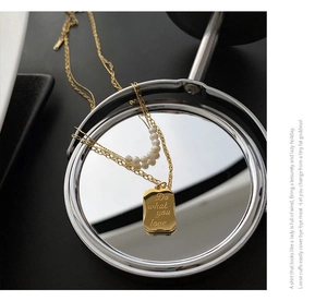 Detail view of double-layer gold necklace with natural pearls and engraved plate