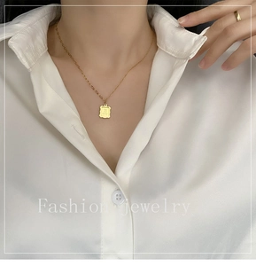 Close-up of golden necklace with a rectangular pendant engraved with Take your memory