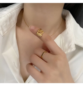 Detail of a gold photo frame pendant necklace and simple ring on a white shirt