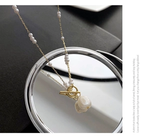 Close-up of gold OT buckle necklace with white baroque pearl pendants on a textured base