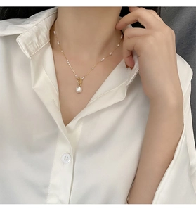 Close-up of a gold pearl necklace on a model wearing a white shirt in natural light