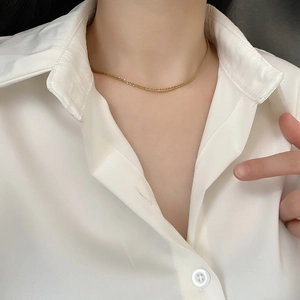 Detail shot of a minimalist gold sparkling choker necklace on a white shirt collar