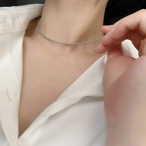 Detail of shimmering silver choker necklace worn with an elegant white shirt on a model
