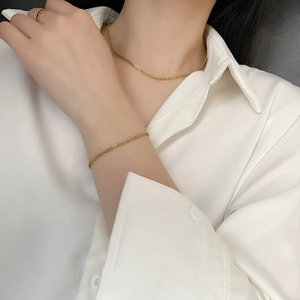 Minimalist sparkling gold chain necklace and bracelet set worn on a white shirt