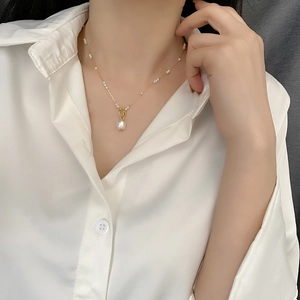 Elegant gold choker featuring small pearls and a baroque pearl pendant on a white silk shirt