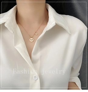 Gros plan d'un collier en or rose avec pendentif double disque gravé de la lettre M
