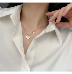 Détail du collier à double pendentif circulaire en or rose avec lettre M gravée sur mannequin