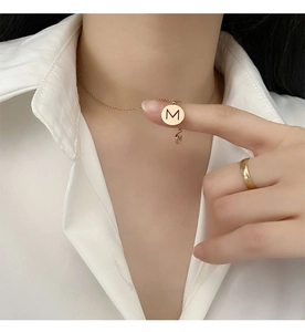 Gros plan du collier avec pendentif lettre M en or rose et bague sur chemise blanche