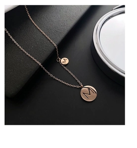 Détail macro du collier en titane or rose avec pendentifs doubles gravés de la lettre M