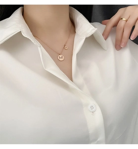 Gros plan du collier double disque lettre M en or rose porté avec une chemise blanche