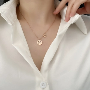 Collier en acier titane or rose avec double pendentif rond lettre M porté sur mannequin