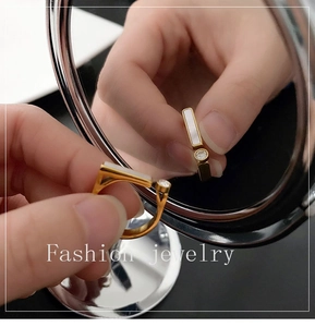 Detail view of a gold shell and zircon open ring reflected in a makeup mirror