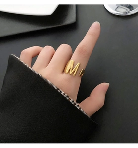 Detail of a bold gold M-shaped ring on index finger with a minimalist fashion aesthetic