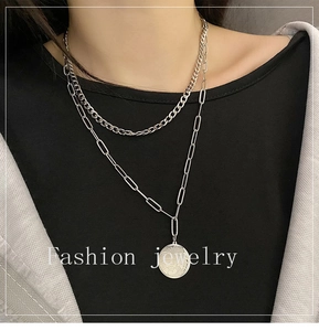 Detail of layered titanium steel necklace with cuban link and portrait coin pendant