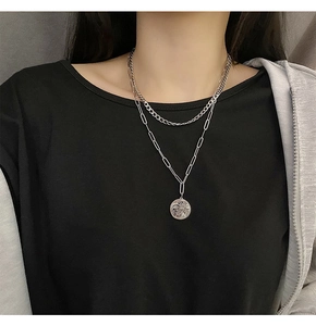 Macro detail of layered silver curb and paperclip chains with coin face pendant