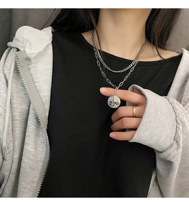 Detail of layered titanium steel necklace with an abstract face coin pendant for women