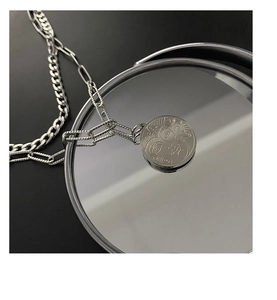 Close-up of a silver titanium steel coin pendant with abstract face on a mirror surface