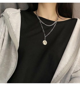 Close-up of double-layered silver chain necklace with a round coin pendant worn by a model