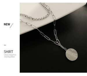 Detail of silver double-layered necklace featuring a Cuban chain and abstract face coin pendant