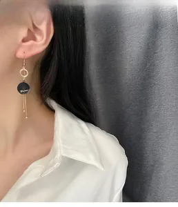 Close-up of long gold tassel earrings with black Love pendant worn by a model