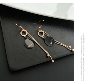Macro detail of rose gold tassel earrings featuring a black circular Love pendant