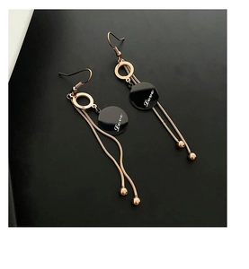 Detail of rose gold tassel earrings with 'Love' engraved black discs on black background