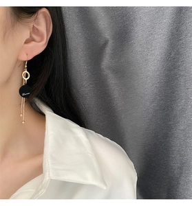 Detail of rose gold long fringe earrings with black Love charm on a model