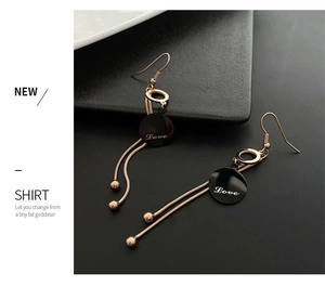 Detail of rose gold tassel earrings with black disc engraved with Love lettering