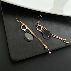Elegant rose gold tassel earrings with black love charm on a modern minimalist backdrop