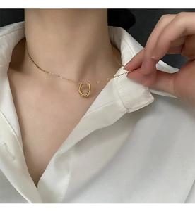 Close-up of polished gold horseshoe U-shaped pendant on a minimalist necklace chain