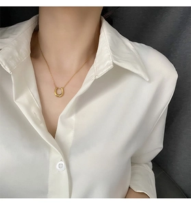Close-up of gold U-shaped pendant necklace worn on a white satin shirt for an elegant look