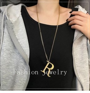 Close-up of a golden letter R pendant necklace styled on a casual dark hoodie sweater