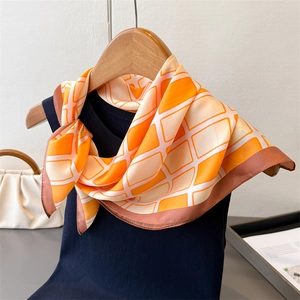 Close-up of orange and white geometric checkered silk scarf styled on a navy blue top