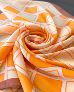 Close-up of orange and beige geometric grid silk scarf with dark brown hemmed edges