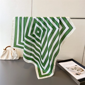 Detail of silk-texture scarf with green geometric patterns draped on a metal rack