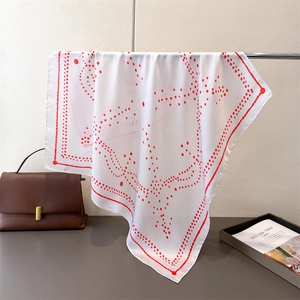 Detail of white silk scarf with red polka dot hearts hanging by a handbag