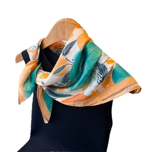Carré de soie élégant aux motifs floraux orange et vert suspendu sur un cintre en bois