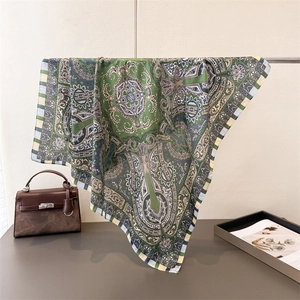 Detail view of retro green paisley silk scarf draped elegantly next to a designer bag